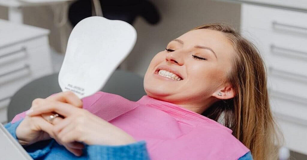 Macquarie Dentists - Woman checking her teeth on the mirror at dentist chair