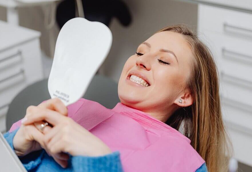 Macquarie Dentists - Woman checking her teeth on the mirror at dentist chair