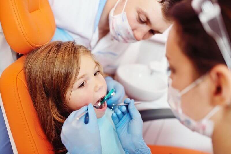 Macquarie Dentists - A child undergoing a routine dental check-up, sitting in a dentist's chair as the dentist inspects her teeth.
