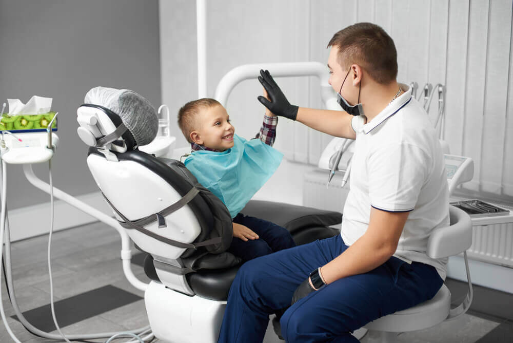 Macquarie Dentists - A young boy sits in a dentist's chair doing high five with dentist